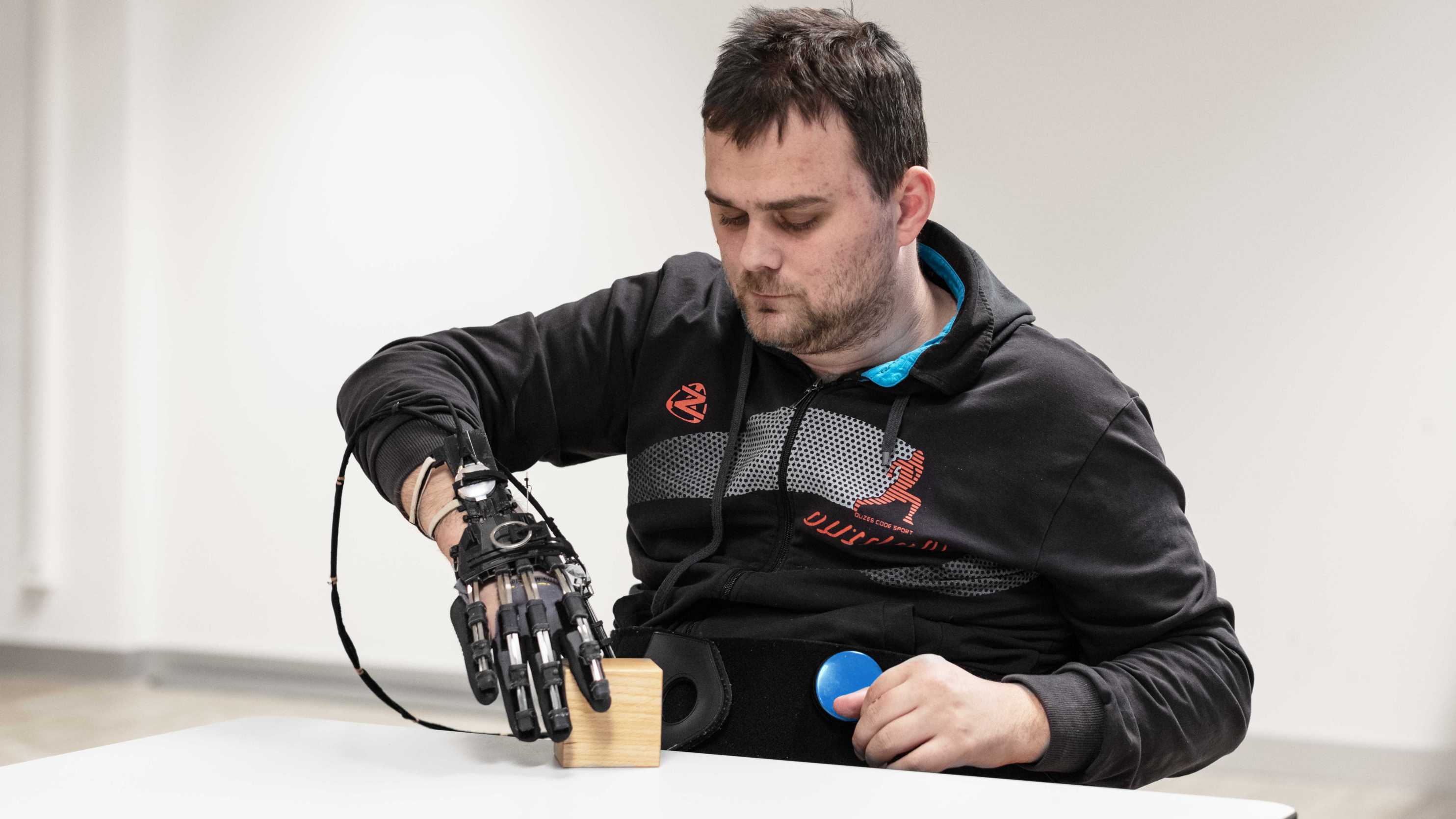 Enlarged view: Person with a hand exoskeleton grasping and lifting a wooden block