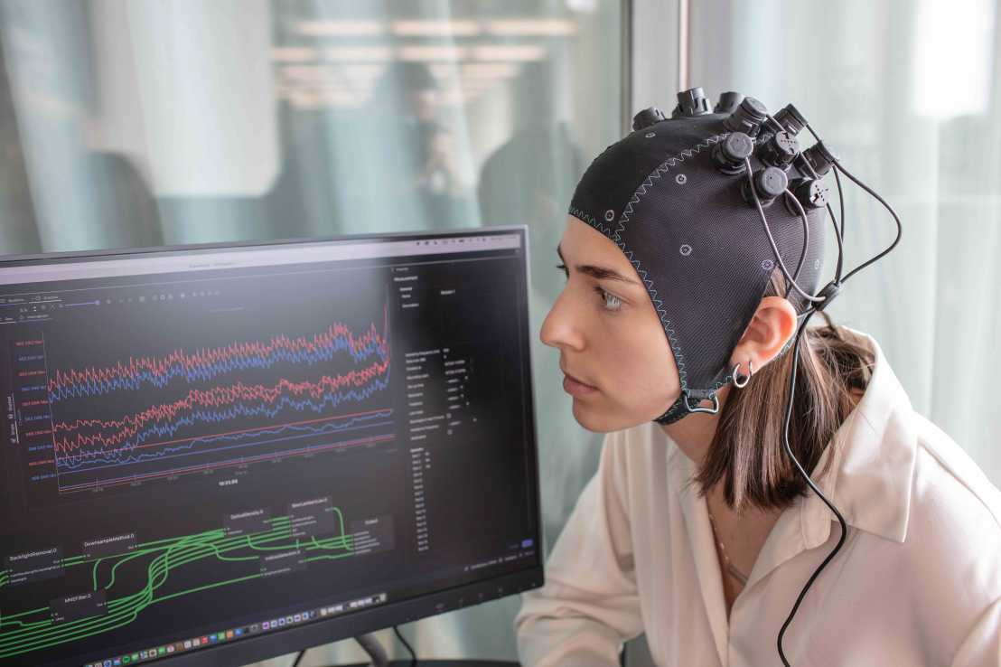 Enlarged view: Woman with fNirs sensors in front of a screen showing brain activity