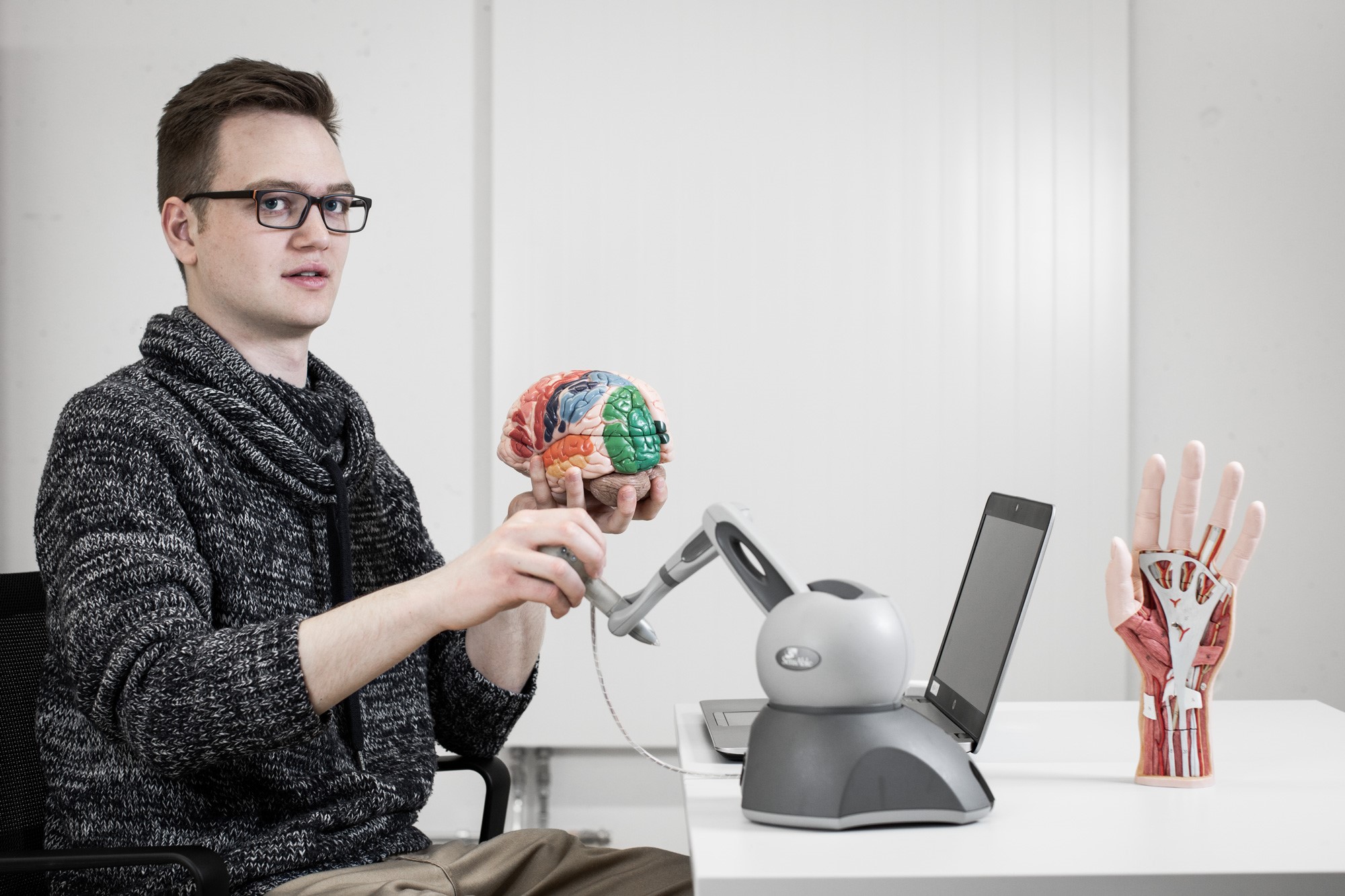 Enlarged view: Chrisoph Kanzler with VPIT device and a stylized artificial brain in his hand. Next to it is a stylized artificial hand in which the components are highlighted in color.