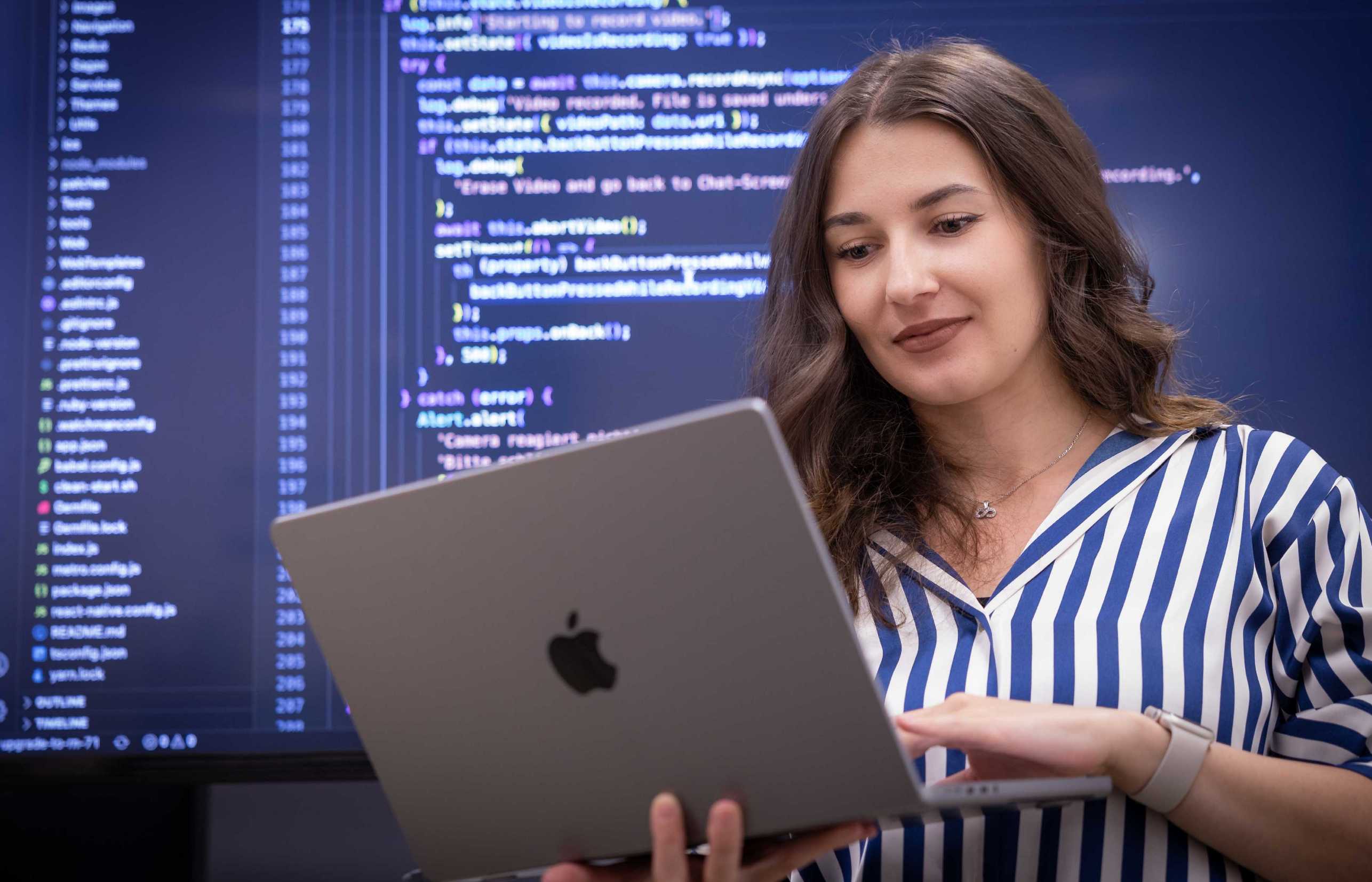 Enlarged view: Alexandra Retevoi working on laptop in front of a huge screen that shows code