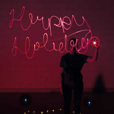 Woman lightpainting the Words Happy Holliday