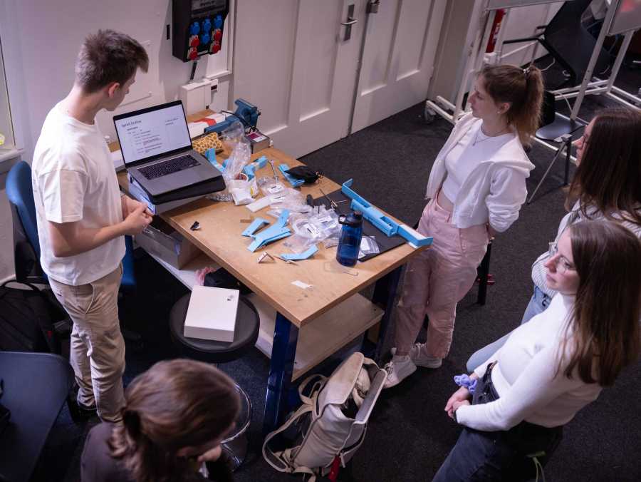 Enlarged view: A group of students standing around a laptop and some blue 3D printed parts.